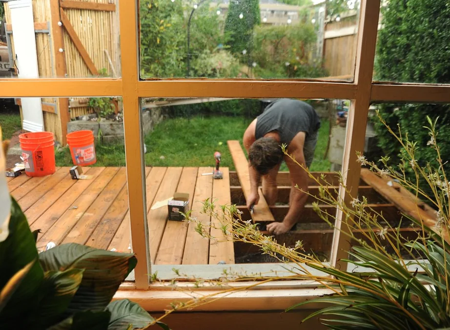 Carpenter kneeling on new deck framing, fitting a board into place