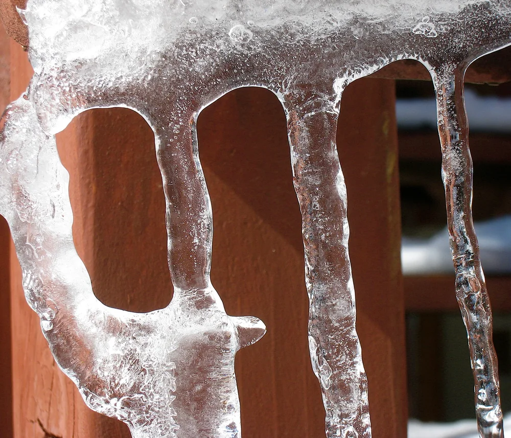 Melting ice hanging from a weathered deck rail in winter sun