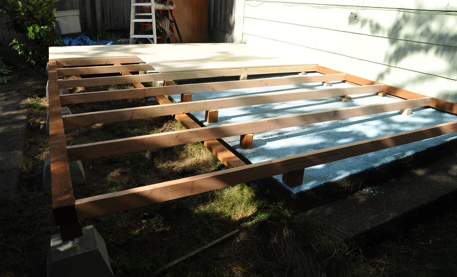 Deck joists set out across concrete pier blocks on a levelled lawn
