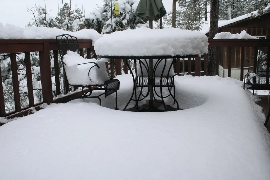 Snow piled deep on a deck table and chairs behind a timber rail