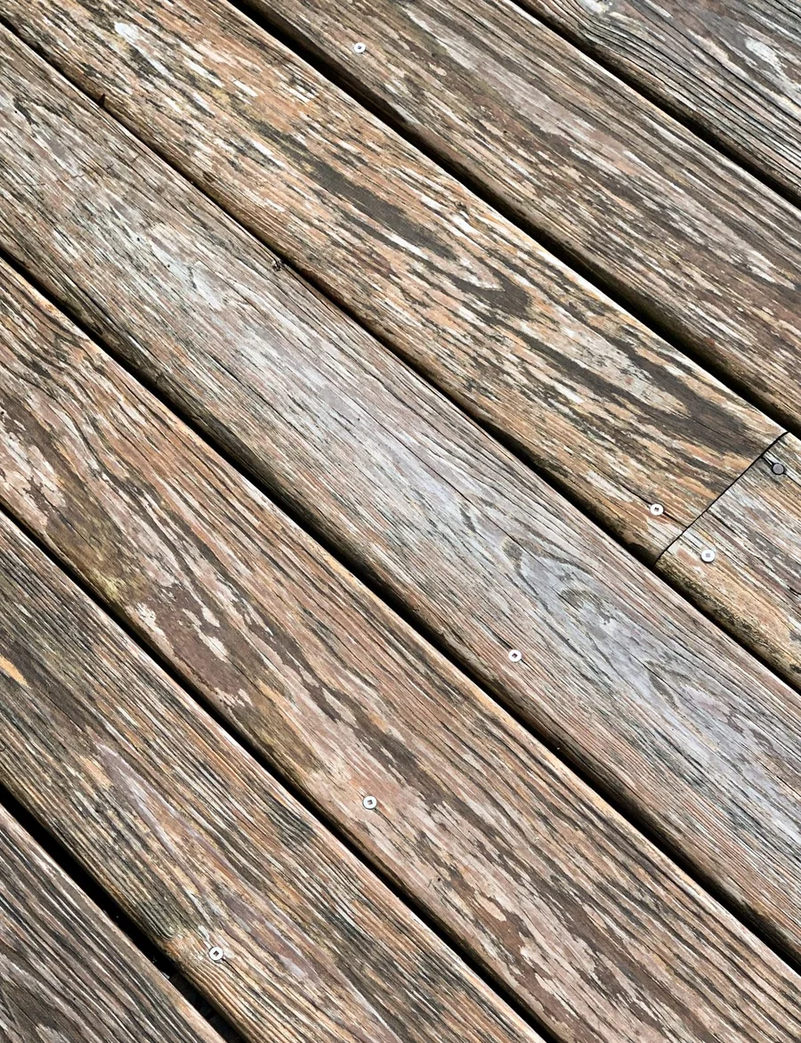 Close view of grey weathered deck boards with raised grain and open checks