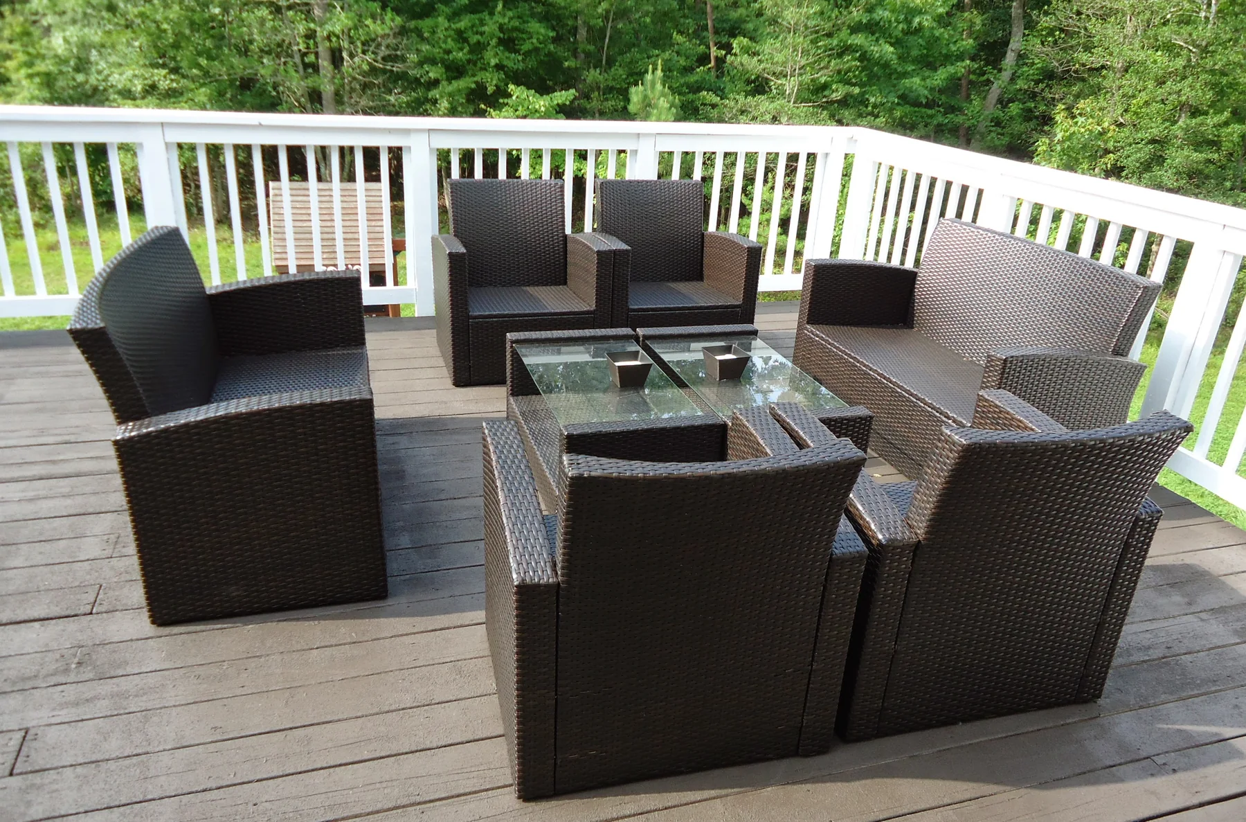 Grey composite deck with white railings and lounge seating beside a wooded yard